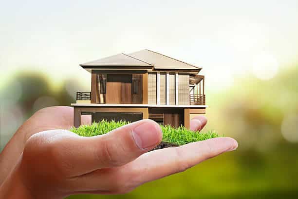 Little brown house with lawn held in two hands for property deeds