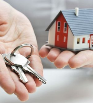 One hand holding keys and one hand holding a little house for transfer of property ownership