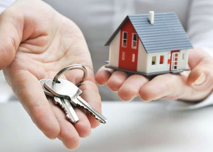 One hand holding keys and one hand holding a little house for transfer of property ownership