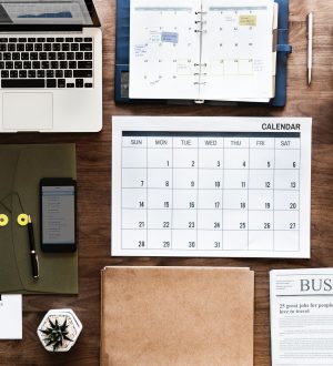 A desk seen from above with a calendar, a phone, a computer and coffee for business organizations