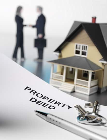 Property deed document with pen and keys with little yellow house in the background and a couple shaking hands in the back ground for real estate law