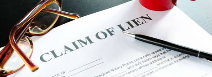 A claim of lien document lays on a table with brown glasses to the left and a black pen to the right for Lien Release